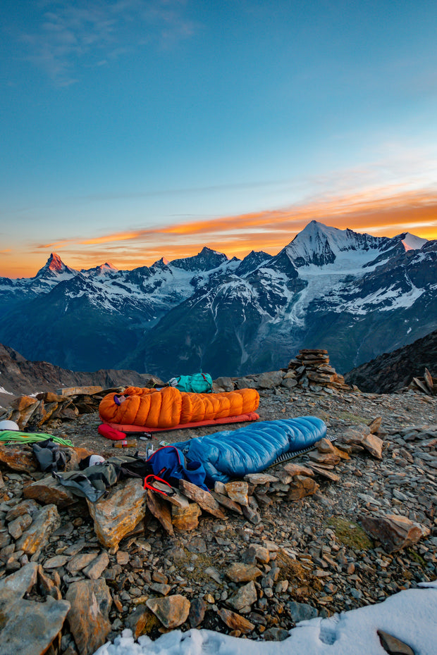 Deux sacs de couchage en bivouac face aux sommets enneigés au coucher du soleil