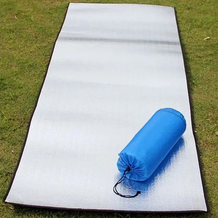 Tapis de sol isolant aluminisé déroulé sur l'herbe, avec son sac de transport